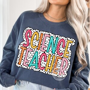 Peut inclure: Un sweat-shirt bleu fonc&eacute; avec un fond &agrave; pois blancs et noirs. Les mots "SCIENCE TEACHER" sont &eacute;crits en lettres color&eacute;es sur le sweat-shirt.