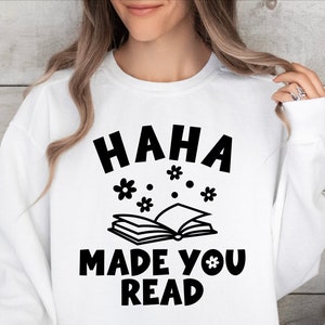 May include: White sweatshirt with black text that reads "HAHA MADE YOU READ" with a book and flowers printed above the text.