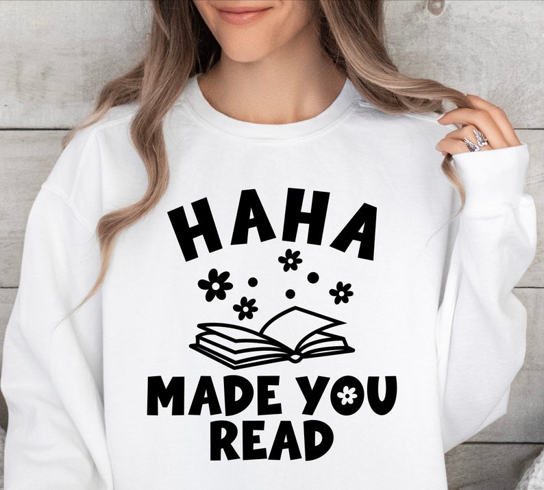 May include: White sweatshirt with black text that reads "HAHA MADE YOU READ" with a book and flowers printed above the text.