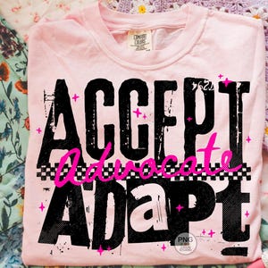 May include: A light pink t-shirt with the words "ACCEPT Advocate ADAPT" in large, distressed black letters. The word "Advocate" is in bright pink script with a checkered pattern. Pink star accents are scattered around the text.