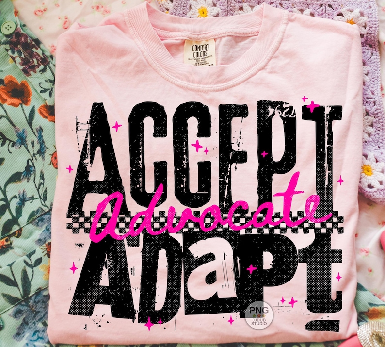 May include: A light pink t-shirt with the words "ACCEPT Advocate ADAPT" in large, distressed black letters. The word "Advocate" is in bright pink script with a checkered pattern. Pink star accents are scattered around the text.