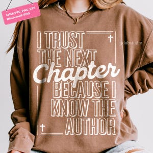 May include: A brown sweatshirt with the text "I TRUST THE NEXT Chapter BECAUSE I KNOW THE AUTHOR" in white. The sweatshirt has a crew neck and long sleeves. The design includes a cross symbol.