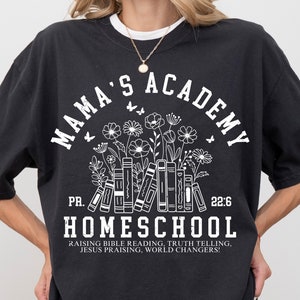 May include: Black t-shirt with white text that reads "Mama's Academy" in a circle with a floral design and books underneath. The text "PR. 22:6" is below the circle and the text "Homeschool" is below that. The text "Raising Bible Reading, Truth Telling, Jesus Praising, World Changers!" is at the bottom of the shirt.
