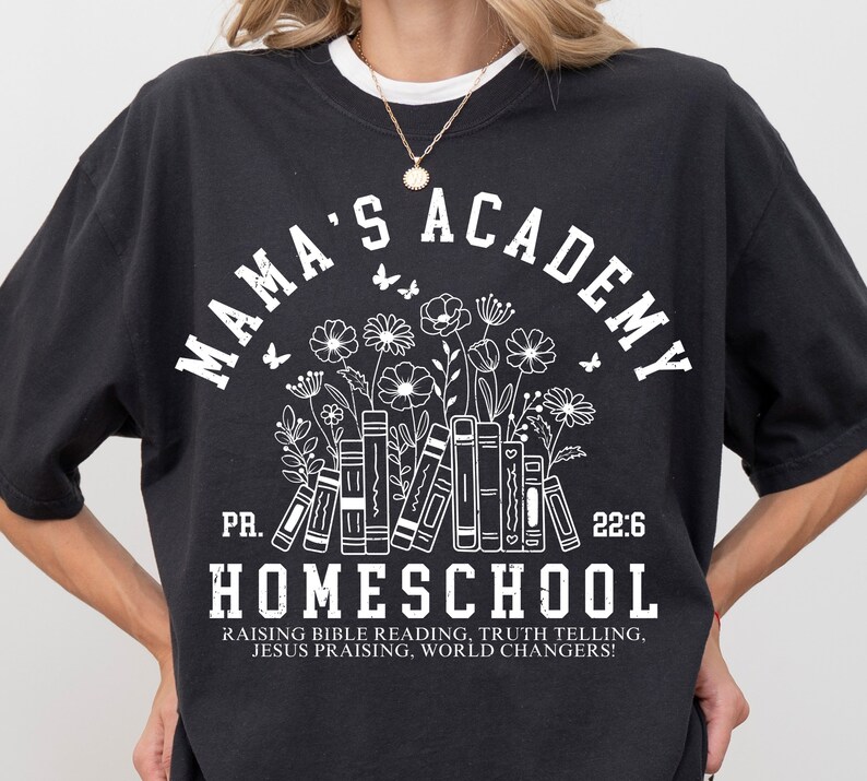 May include: Black t-shirt with white text that reads "Mama's Academy" in a circle with a floral design and books underneath. The text "PR. 22:6" is below the circle and the text "Homeschool" is below that. The text "Raising Bible Reading, Truth Telling, Jesus Praising, World Changers!" is at the bottom of the shirt.