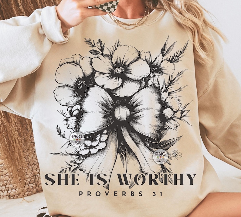 Peut inclure: Un sweat-shirt beige avec un motif floral noir et blanc et un n&oelig;ud. Le texte "She is Worthy Proverbs 31" est imprim&eacute; en bas du sweat-shirt.