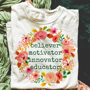 以下が含まれることがあります： 「believer, motivator, innovator, educator」の緑色の文字と花のリースデザインが特徴のクリーム色のTシャツ。 リースにはピンクとオレンジの花と緑の葉が含まれています。 シャツは折りたたまれています。