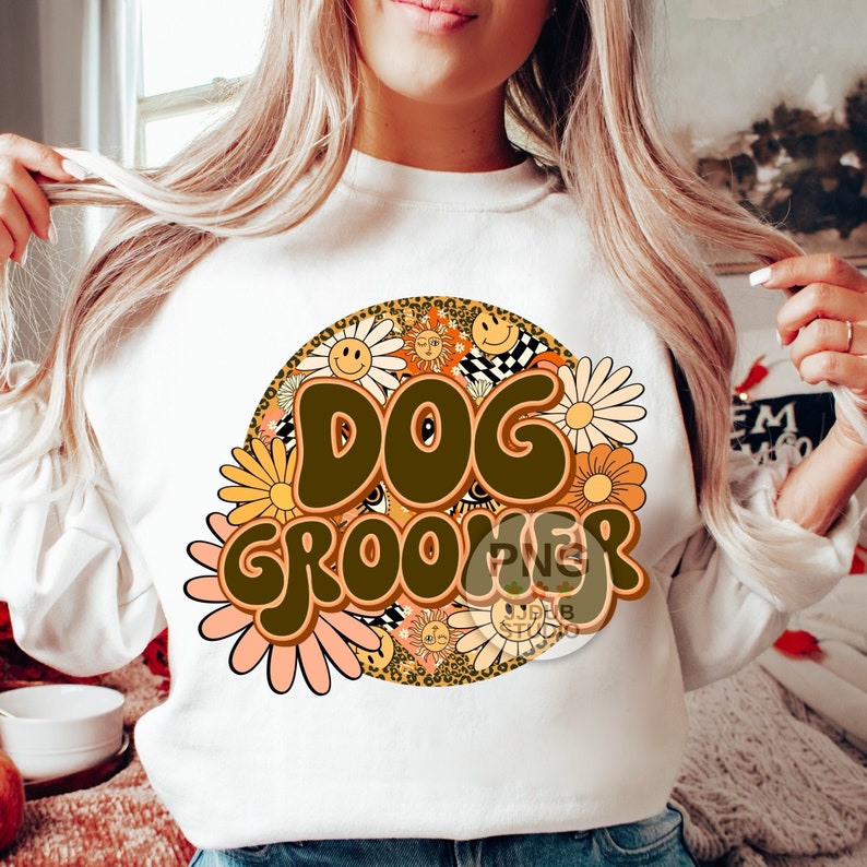 May include: White sweatshirt with a brown and orange graphic design of the words "Dog Groomer" surrounded by flowers and smiley faces.