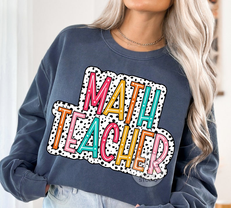 Op de afbeelding: Een marineblauw sweatshirt met een kleurrijke afbeelding waarop "MATH TEACHER" staat in een wit en zwart stippenpatroon.