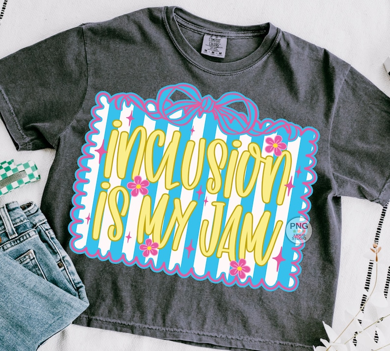 May include: Dark gray t-shirt with the phrase "INCLUSION IS MY JAM" in yellow script. The text is set against a blue and white striped background, framed by a pink scalloped border and adorned with pink flowers and stars.