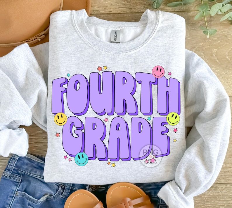 May include: A light grey sweatshirt with the text "FOURTH GRADE" in purple letters with a 3D effect. The letters are surrounded by colorful stars and smiley faces.