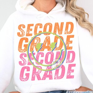 May include: White hoodie with a distressed graphic design that says "Second Grade" in orange, pink, and blue. The graphic includes a lightning bolt and a smiley face.