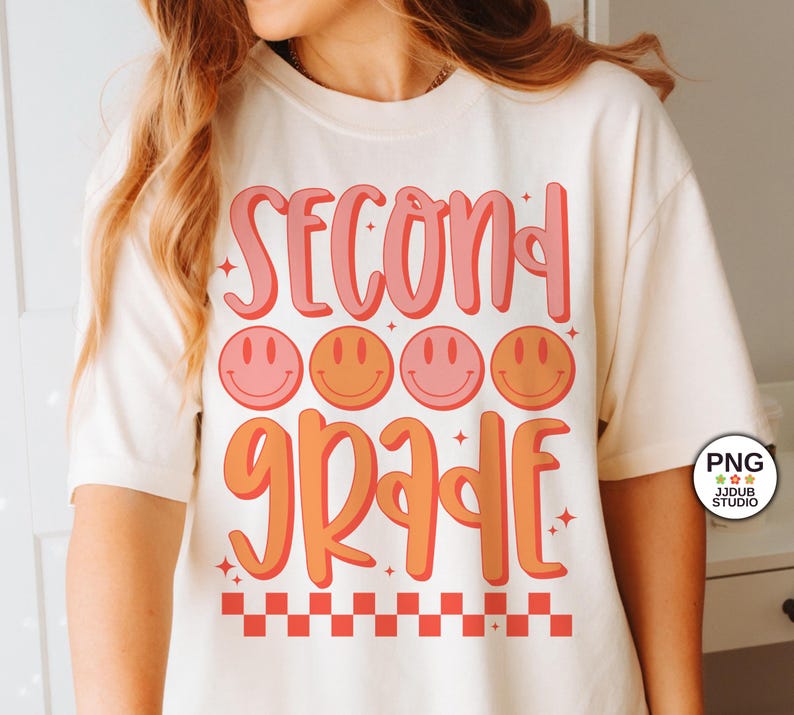 May include: A white t-shirt with the text "Second Grade" in pink and orange lettering. The text is surrounded by four orange and pink smiley faces. The bottom of the shirt has a red and white checkered pattern.