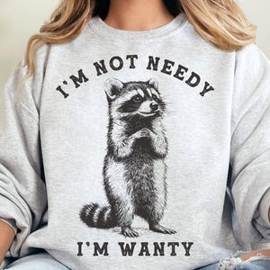 May include: Grey sweatshirt with a black and white illustration of a raccoon and the text "I'm not needy I'm wanty".