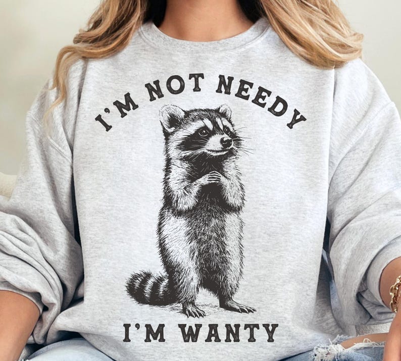 May include: Grey sweatshirt with a black and white illustration of a raccoon and the text "I'm not needy I'm wanty".