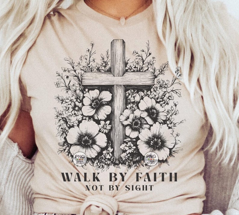 Peut inclure: Un t-shirt beige avec un motif noir et blanc d'une croix entour&eacute;e de fleurs. Le texte "Walk by Faith Not by Sight" est imprim&eacute; sous le motif.