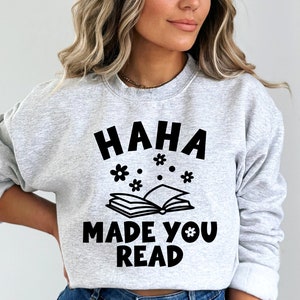 May include: Gray sweatshirt with the text "HAHA MADE YOU READ" in black lettering. The text is surrounded by small black flower illustrations.