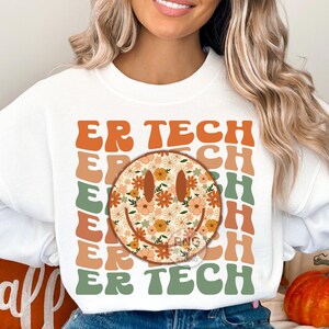 May include: White sweatshirt with the text "ER TECH" repeated in a retro style with a floral smiley face in the center.