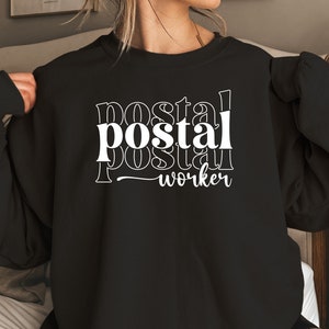 May include: Black sweatshirt with white text that reads "postal worker" in a layered, stacked font.