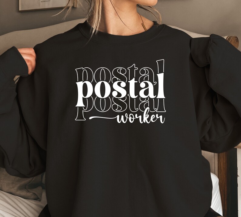 May include: Black sweatshirt with white text that reads "postal worker" in a layered, stacked font.
