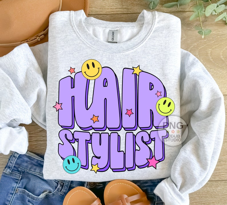 May include: A light gray sweatshirt with a purple and yellow graphic design that says "Hair Stylist" with smiley faces and stars.