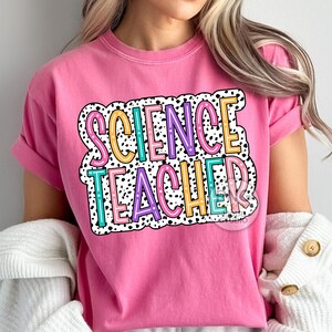 Peut inclure: T-shirt rose avec le texte "SCIENCE TEACHER" dans une police color&eacute;e, soulign&eacute;e avec des pois noirs.