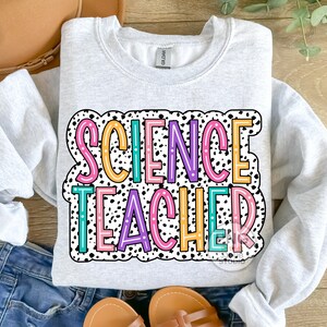 Peut inclure: Un sweat-shirt gris avec un fond &agrave; pois noir et blanc. Les mots "SCIENCE TEACHER" sont &eacute;crits en lettres color&eacute;es avec un contour blanc.