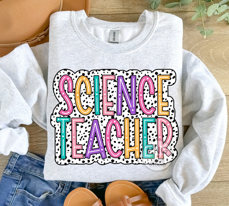Peut inclure: Un sweat-shirt gris avec un fond &agrave; pois noir et blanc. Les mots "SCIENCE TEACHER" sont &eacute;crits en lettres color&eacute;es avec un contour blanc.