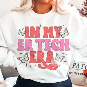 May include: White sweatshirt with pink and red text that reads "In My ER Tech Era" with butterfly graphics.
