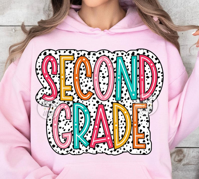 May include: Pink hoodie with a black and white polka dot background and the text "SECOND GRADE" in colorful letters with a white outline.