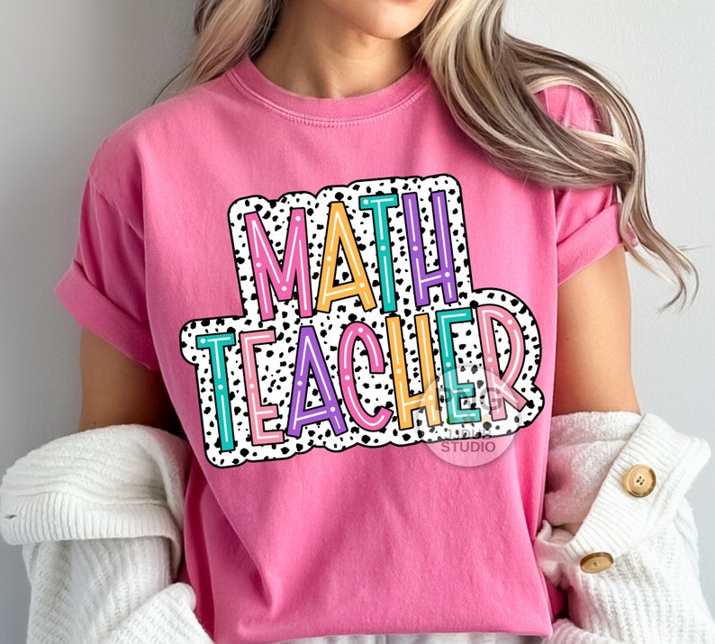Op de afbeelding: Roze T-shirt met de tekst "MATH TEACHER" in een kleurrijk, retro-lettertype met zwarte stippen.