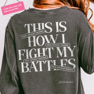 以下が含まれることがあります： 「THIS IS HOW I FIGHT MY BATTLES」の白文字がプリントされた、濃いグレーの長袖シャツ。「PRAY WITHOUT CEASING」の文字が上下に配置されています。シャツはヴィンテージ風の外観です。