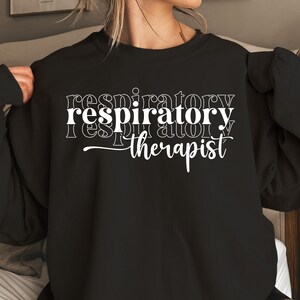 K&ouml;nnte beinhalten: Schwarzer Pullover mit wei&szlig;em Text, der "respiratory therapist" in einem gestapelten, &uuml;berlappenden Design lautet.