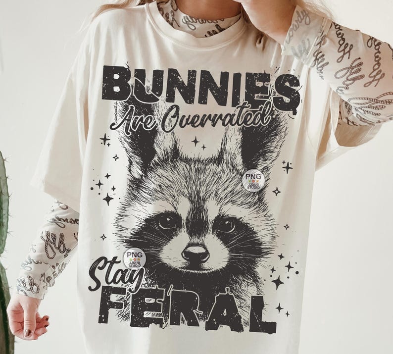 K&ouml;nnte beinhalten: Ein wei&szlig;es T-Shirt mit einer schwarzen Grafik eines Waschb&auml;ren mit dem Text "Bunnies Are Overrated Stay Feral".