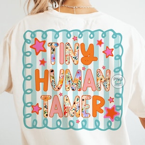 以下が含まれることがあります： クリーム色のTシャツにカラフルなグラフィック。グラフィックは、オレンジとピンクで「TINY HUMAN TAMER」という言葉を特徴とし、文字には花のパターンがあります。デザインは星が付いたターコイズのボーダーで囲まれています。