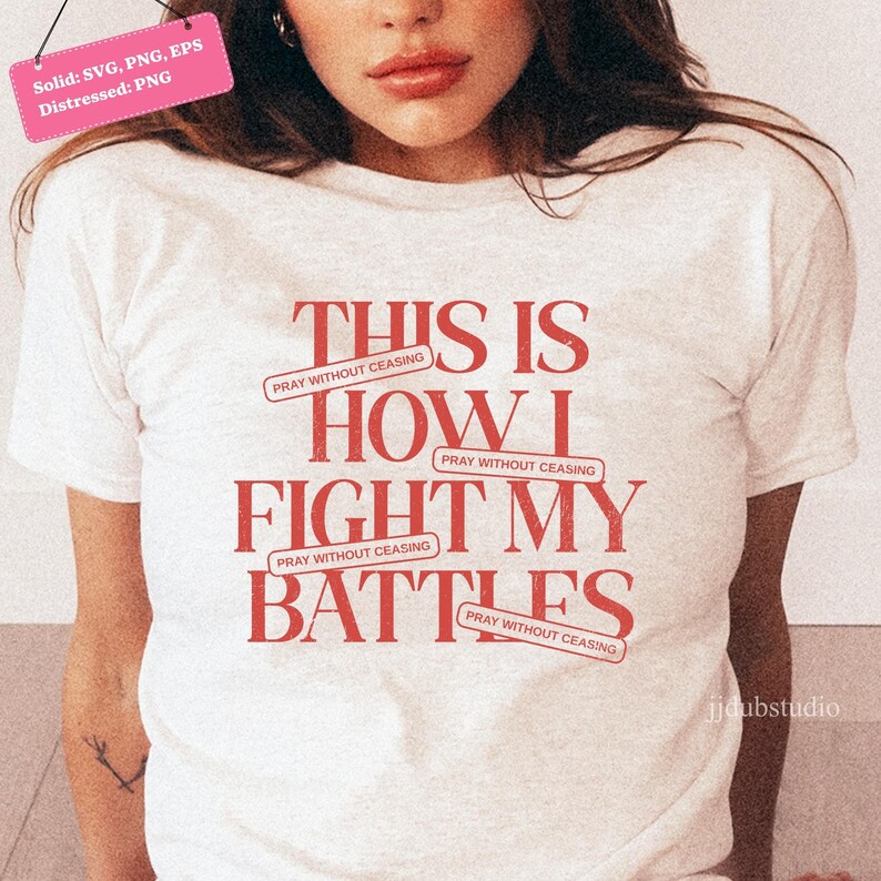 以下が含まれることがあります： 「THIS IS HOW I FIGHT MY BATTLES」の赤い文字がプリントされた白いTシャツ。「PRAY WITHOUT CEASING」の文字が上下に配置されています。半袖でクルーネックのデザインです。