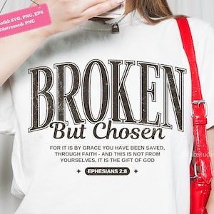 May include: White t-shirt with the text "BROKEN But Chosen" in a distressed, dark brown font. Below the main text is the phrase "FOR IT IS BY GRACE YOU HAVE BEEN SAVED, THROUGH FAITH - AND THIS IS NOT FROM YOURSELVES, IT IS THE GIFT OF GOD EPHESIANS 2:8".