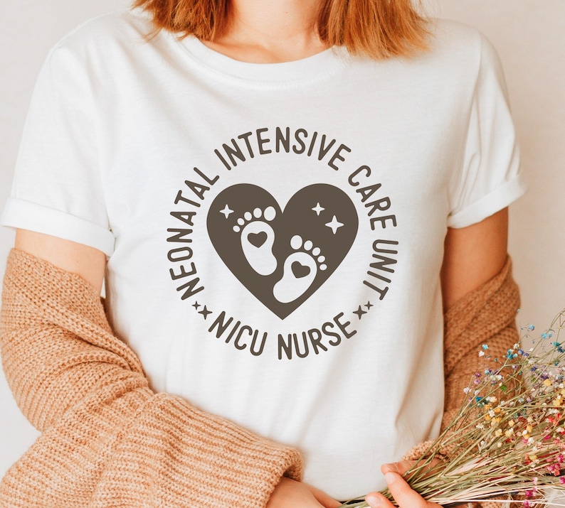 May include: White t-shirt featuring a circular design with the text "Neonatal Intensive Care Unit NICU Nurse." The design includes a heart shape with baby footprints and stars. The shirt is a casual style.