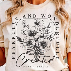 Peut inclure: Un t-shirt beige avec un motif graphique noir repr&eacute;sentant un bouquet de fleurs et le texte "Fearfully and Wonderfully Created Psalm 139:14".