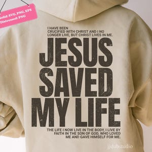 Może przedstawiać: Beżowa bluza z kapturem z napisem "JESUS SAVED MY LIFE" dużymi, zniszczonymi, ciemnobrązowymi literami. Nad tekstem znajdują się słowa "I HAVE BEEN CRUCIFIED WITH CHRIST AND I NO LONGER LIVE, BUT CHRIST LIVES IN ME."