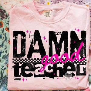 以下が含まれることがあります： 黒とピンクで「DAMN good teacher」と書かれた、薄いピンク色のTシャツ。テキストは、市松模様とピンクの星のアクセントが付いた、使い古されたような外観です。