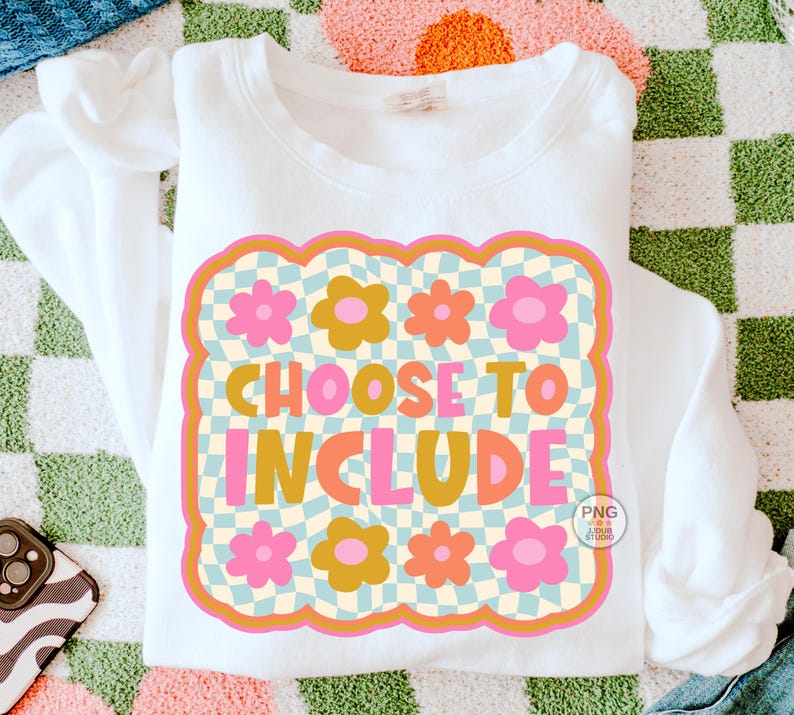 May include: White sweatshirt with a retro design that says "CHOOSE TO INCLUDE". The design features a checkered background, flowers, and a wavy border in shades of pink, orange, and yellow. The sweatshirt is on a colorful patterned surface.