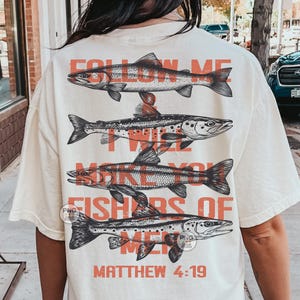 May include: A cream-coloured t-shirt with four detailed fish illustrations in black and red, stacked vertically. The text "FOLLOW ME I WILL MAKE YOU FISHERS OF MEN" and "MATTHEW 4:19" are printed in red.