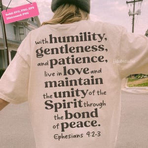 以下が含まれることがあります： 黒いテキストデザインのクリーム色のTシャツ。テキストには「謙虚さ、優しさ、忍耐、愛、統一、精神、絆、平和」という言葉と聖書の節エペソ4：2-3が含まれています。シャツは人が着ています。