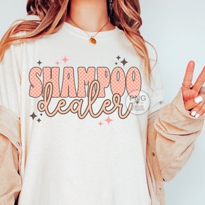 May include: A white t-shirt with the text "SHAMPOO dealer" in pink and brown letters with a checkered pattern. The text is surrounded by small pink and black stars.