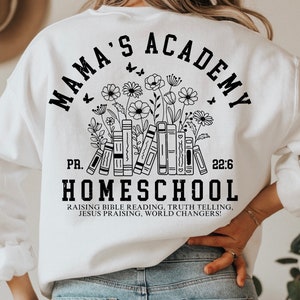 May include: White sweatshirt with black text that reads "Mama's Academy" in a circle with a floral design and books underneath. The text "PR. 22:6 HOMESCHOOL" is below the circle. The text "Raising Bible Reading, Truth Telling, Jesus Praising, World Changers!" is below the text "HOMESCHOOL".