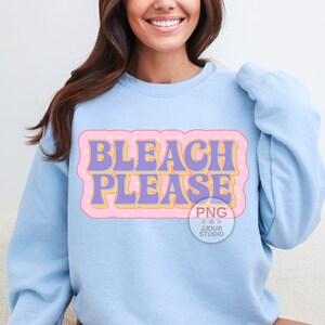 May include: A light blue sweatshirt with the text "Bleach Please" in a retro style font with yellow and purple accents on a pink background.