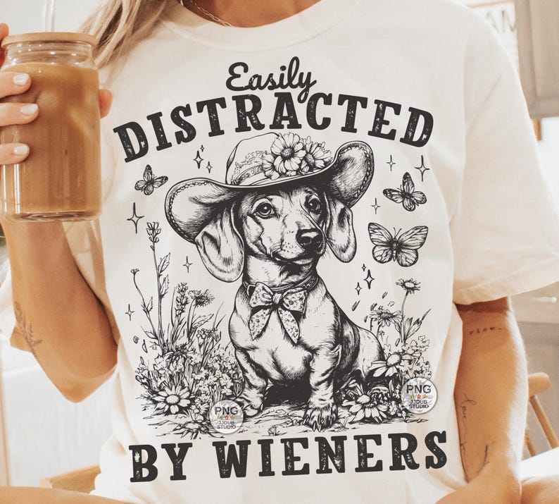 May include: White t-shirt with a black and white illustration of a dachshund wearing a flower crown and the text "Easily Distracted By Wieners".