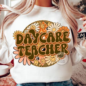Peut inclure: Sweat-shirt blanc avec un motif r&eacute;tro repr&eacute;sentant un cercle de fleurs color&eacute;es et le texte "Daycare Teacher" en lettres brunes.