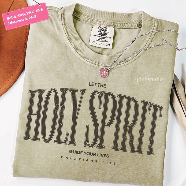 以下が含まれることがあります： 薄緑色のTシャツ。 ぼろぼろの茶色の文字で「LET THE HOLY SPIRIT」と書かれています。 シャツには「GUIDE YOUR LIVES GALATIANS 5:16」というテキストも含まれています。 ピンクのペンダントが付いたシルバーのネックレスがシャツの上にあります。