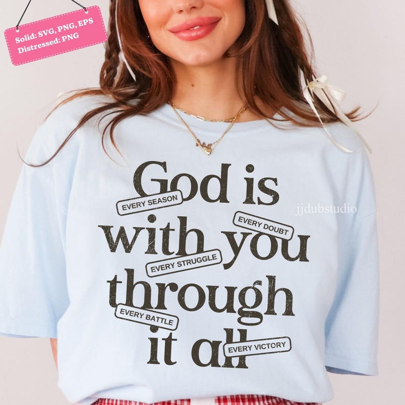 May include: Light blue t-shirt with the message "God is with you through it all" in black text. The text includes phrases like "Every Season," "Every Doubt," and "Every Victory." The shirt has a distressed design.